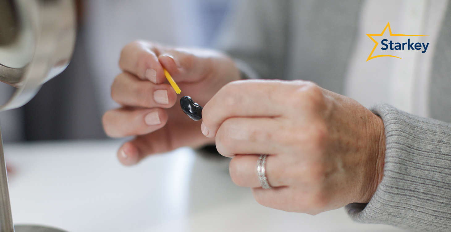 Close-up of two hands changing the wax guard on a hearing aid