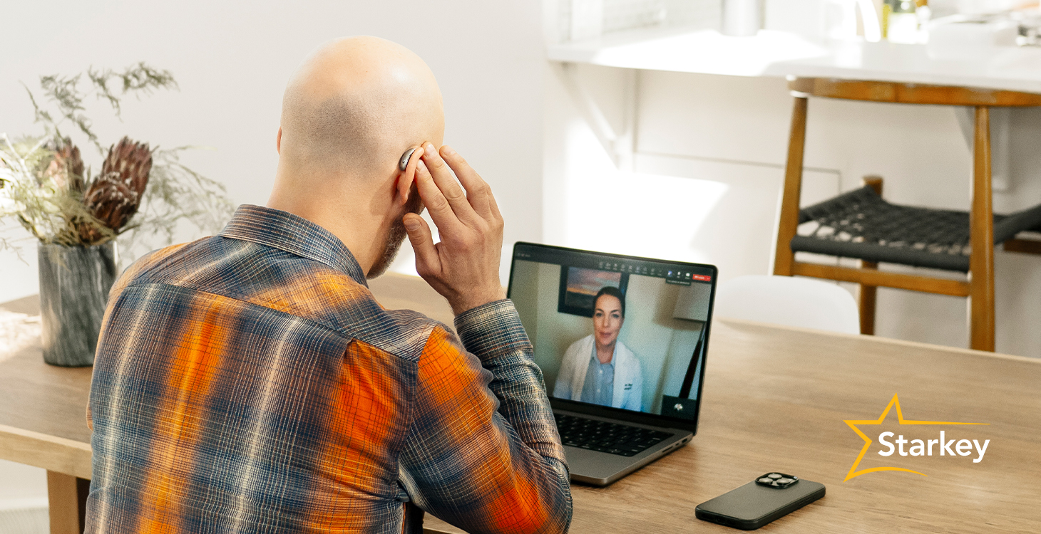 Image of hearing aid wearer touching side of hearing aid while on a laptop call